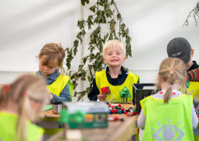 Woodsculpture Børn i neonvest deltager i udendørs aktivitet ved event.