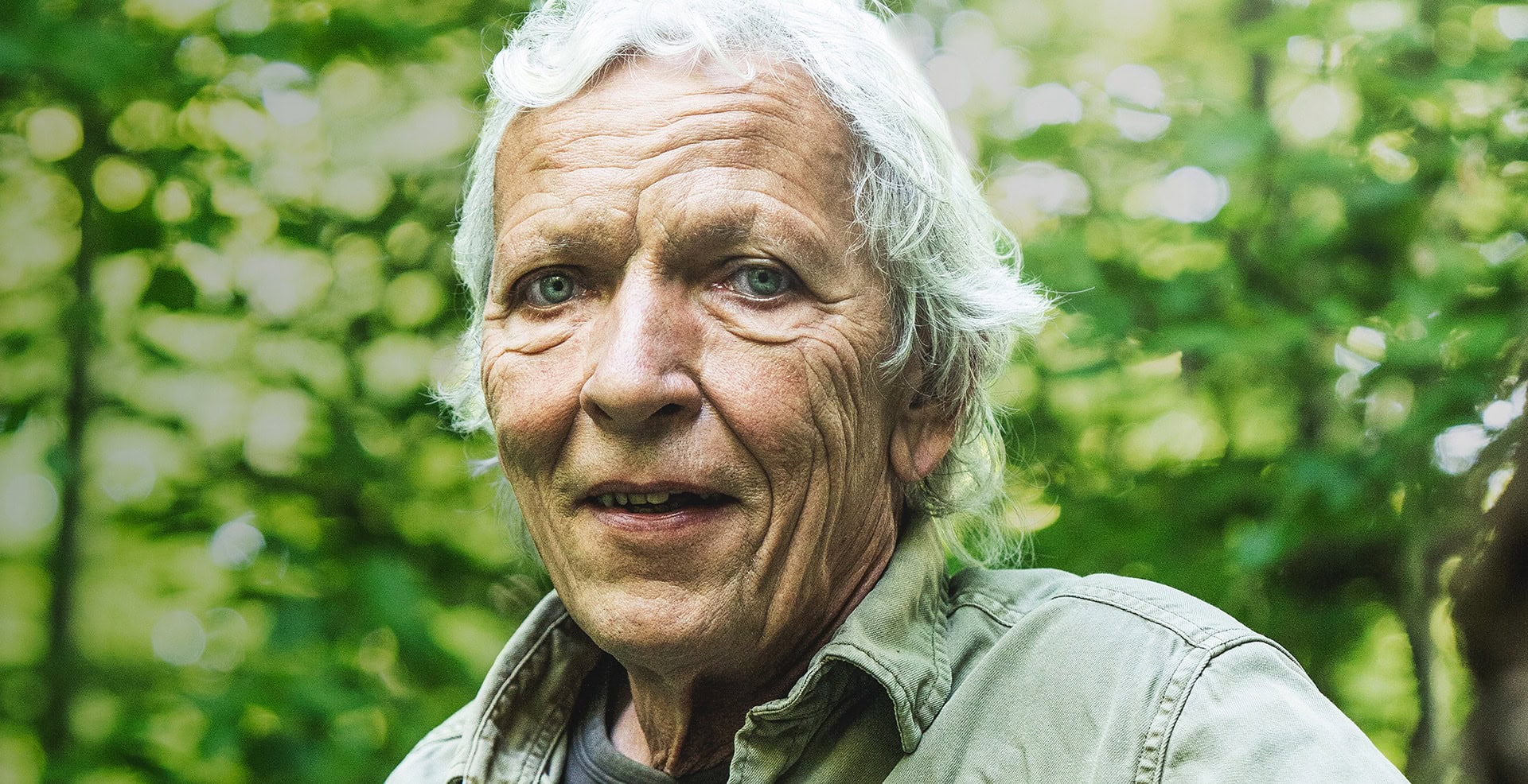 Jørgen Skouboe i naturen Ældre mand i naturen med gråt hår og grøn baggrund.