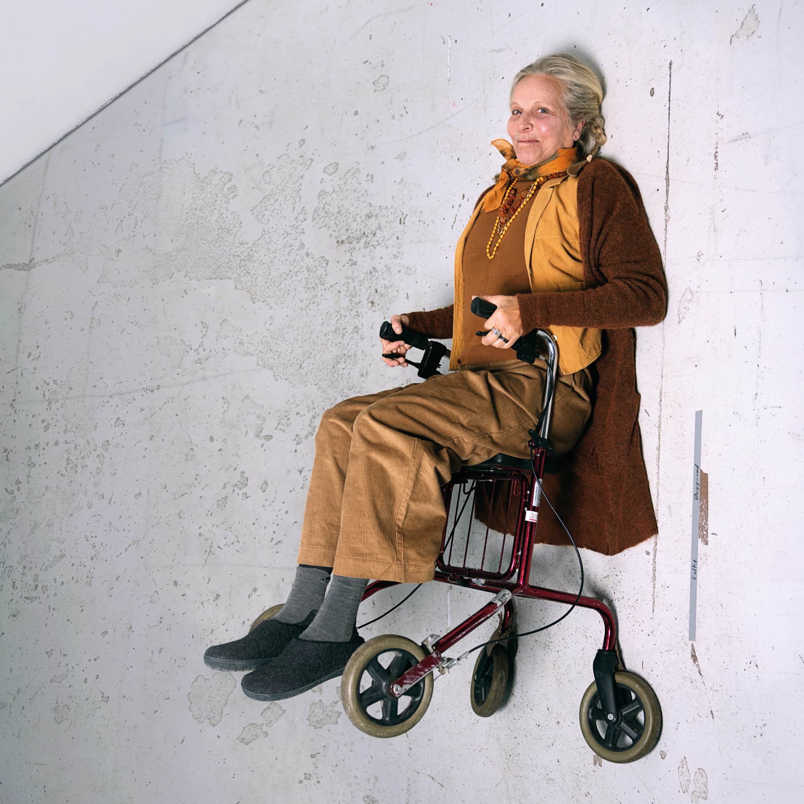 Eldre kvinde bruger rollator, smilende, i indendørs miljø.