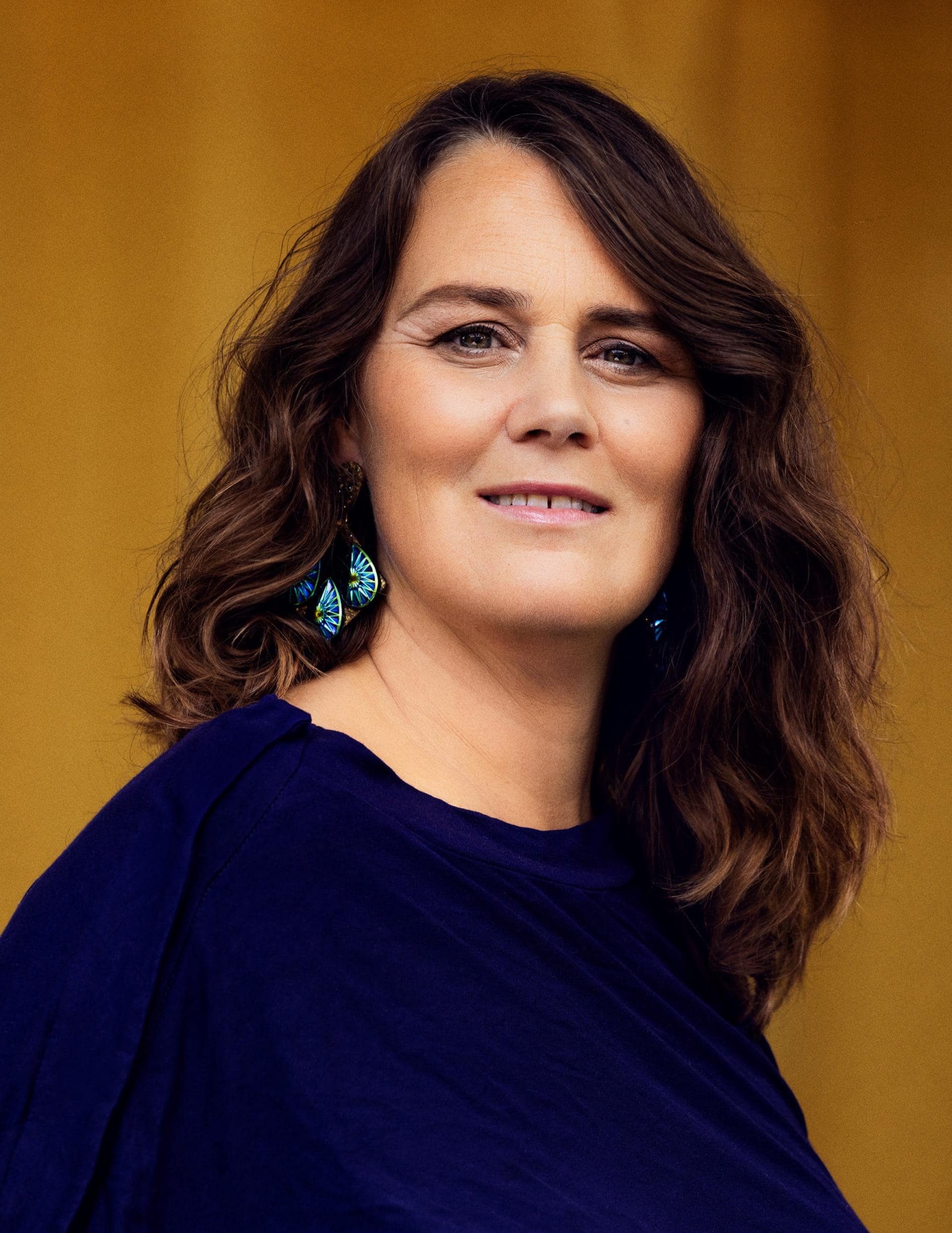 Johanne Mygind smilende portræt med blå tøj og øreringe.
