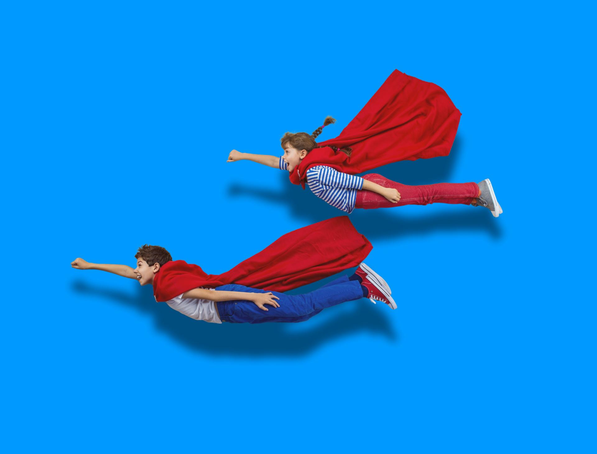 Børn som superhelte i leg To børn i superheltekostumer flyver mod en blå baggrund.